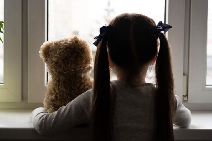 child with teddy bear looking out of the window