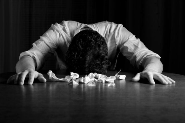 man with head on table in front of crumpled paper