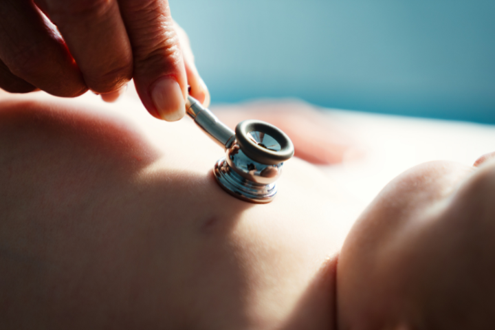 A hand holds a stethoscope to a baby's chest