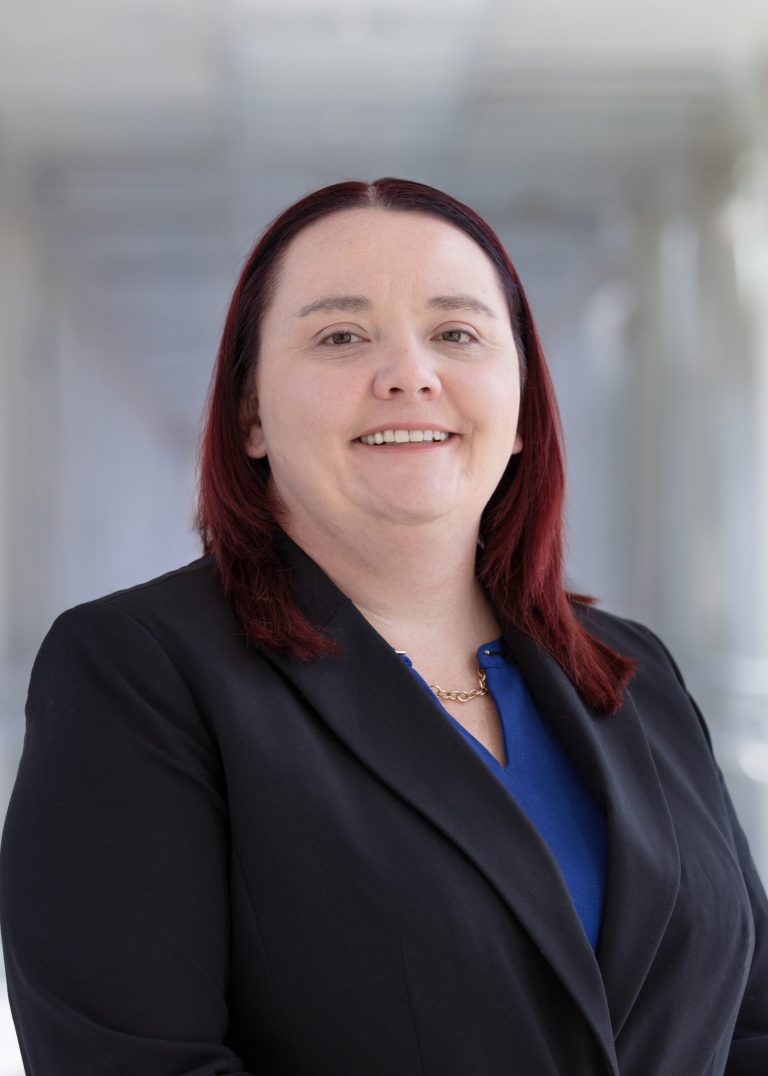 Professional headshot of VPLC employee Jessica Conley, who has long red hair and is wearing a black jacket with a blue shirt underneath.