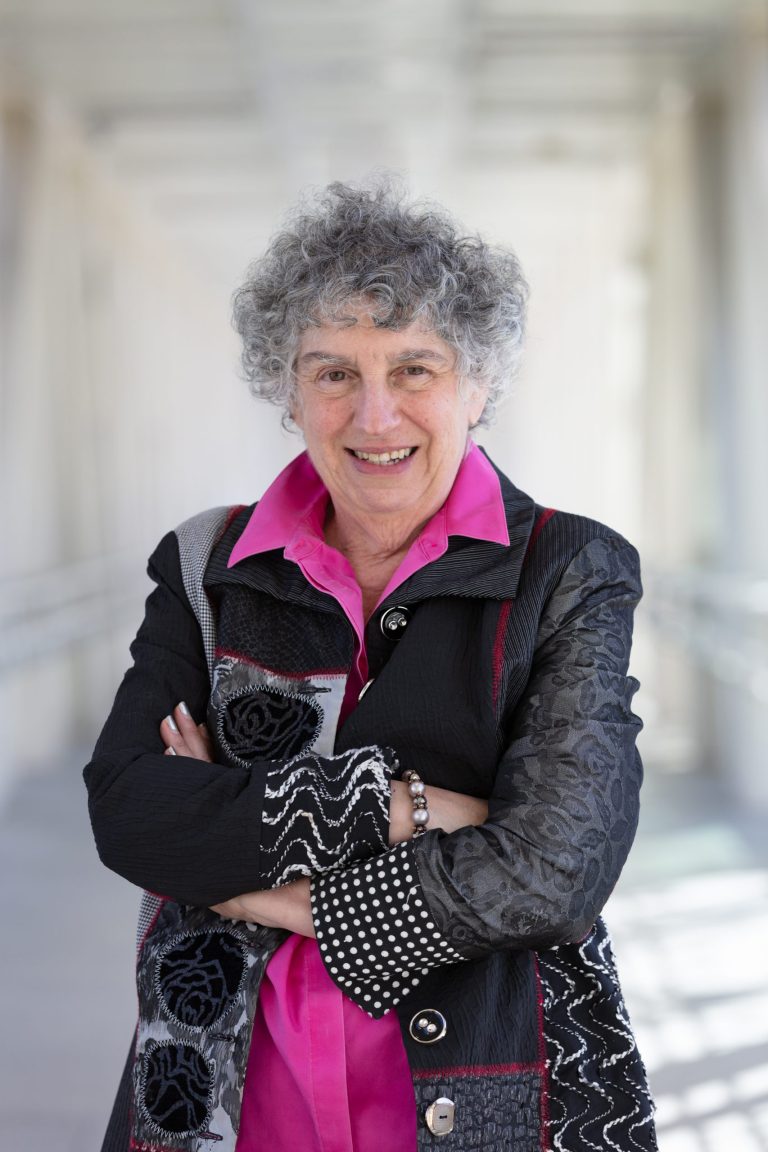 Professional headshot of VPLC employee Lois Caliri, who has short, curly gray hair and is wearing a black and white patterned jacket with a hot pink button down shirt underneath.