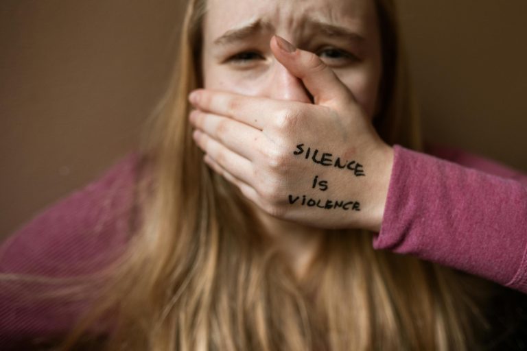 woman covering her mouth, her hand reads silence is violence
