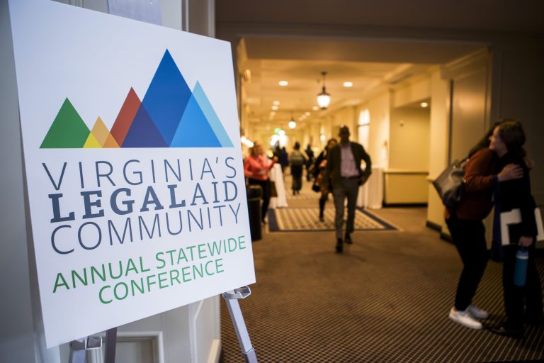 A sign for "Virginia's Legal Aid Community Annual Statewide Conference" is displayed, with participants mingling in a hallway in the background.