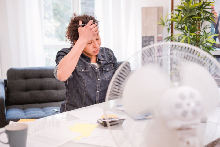 Someone sitting behind a fan, with their hand to their head