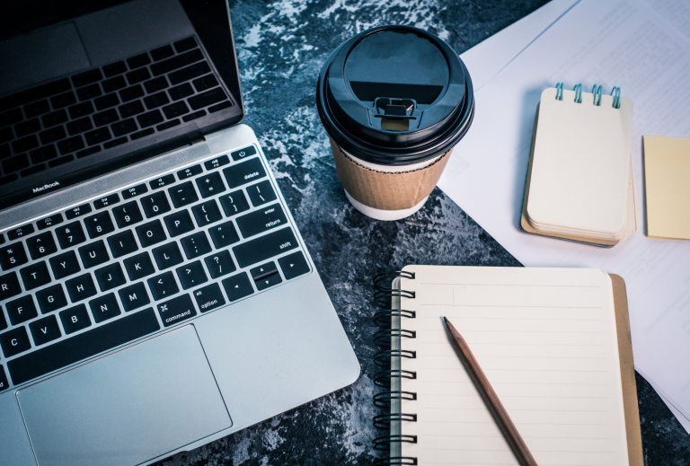 A picture of a laptop with a coffee and notepad on a desk