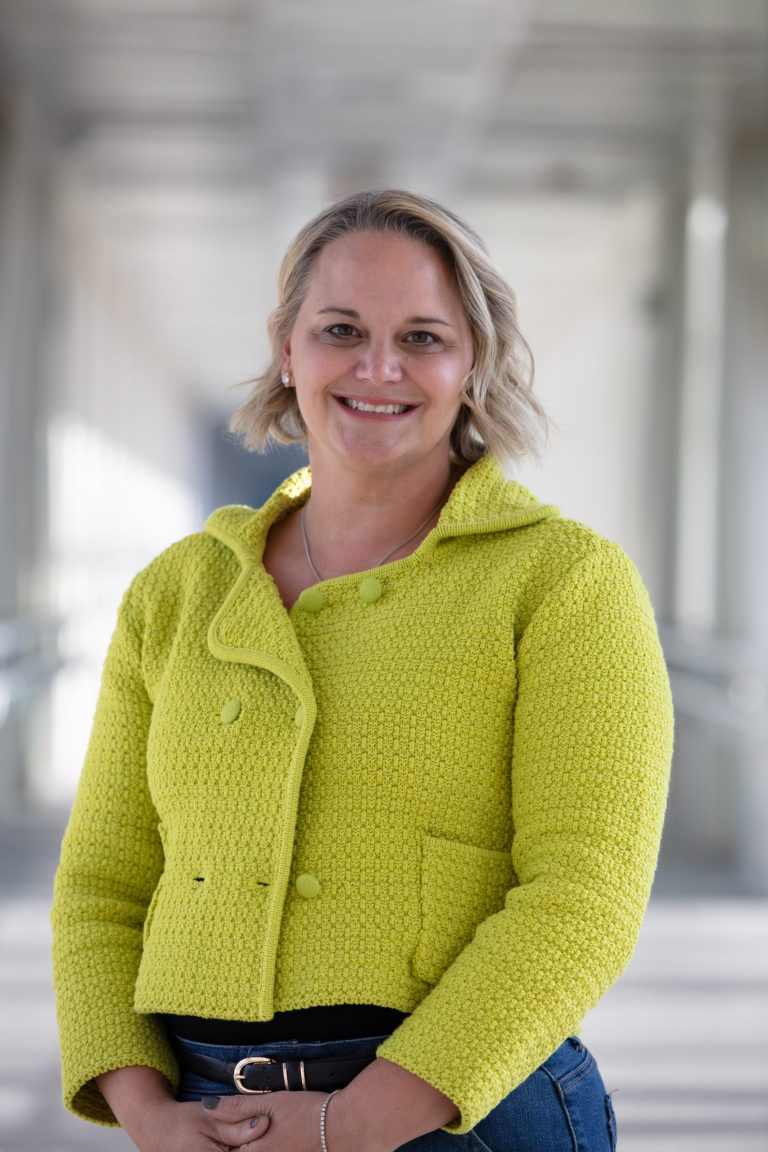 Professional headshot of VPLC employee Faith Kallman, who has chin-length, wavy blonde hair and is wearing a long sleeved, neon yellow dress shirt.